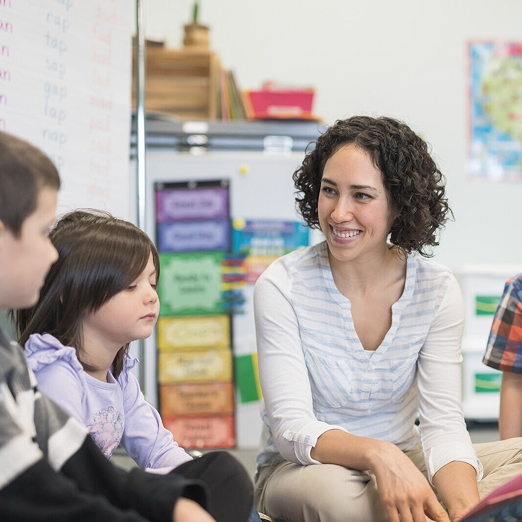 Lehrerin sitzt inmitten von Grundschülern im Kreis